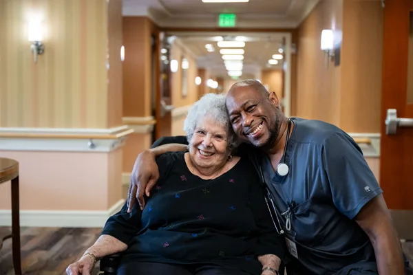 Edenwald_Health-Services_Assisted-Living A male nurse embracing an elderly patient in a wheelchair
