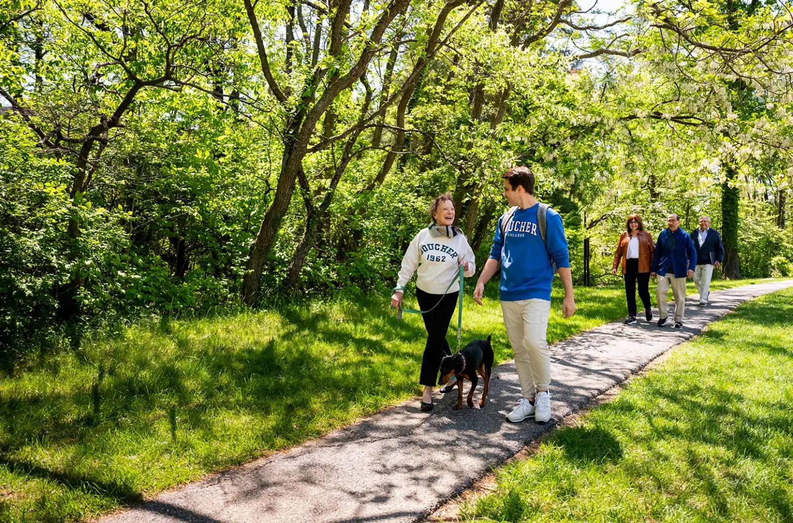 A senior woman walking a dog on a college campus with a young male student