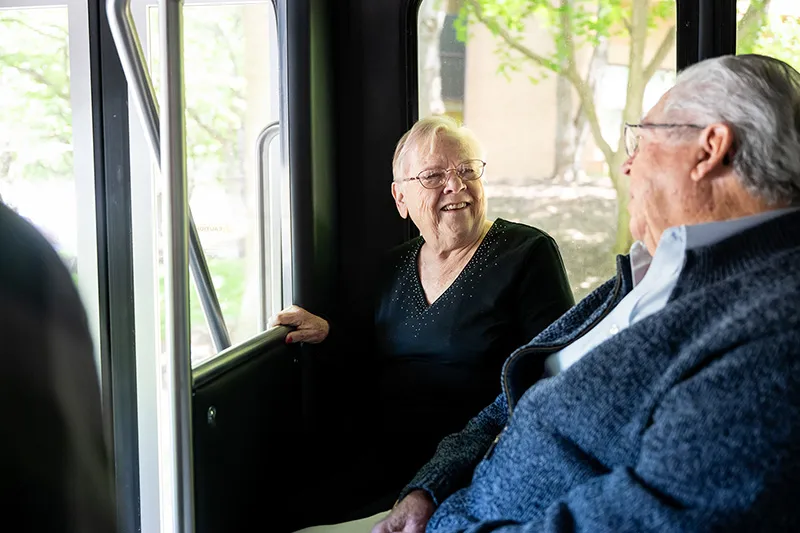 An elderly man and woman smiling and talking on a shuttle bus