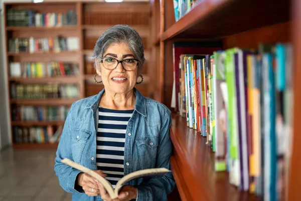 A senior woman in a library holding a book