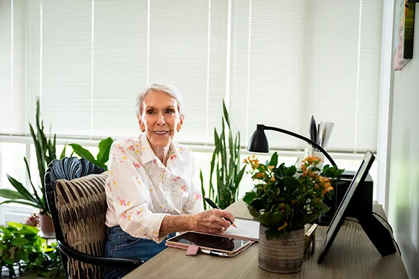 Edenwald_Health-Services_Independent-Living A senior woman sitting at a desk taking notes with a tablet