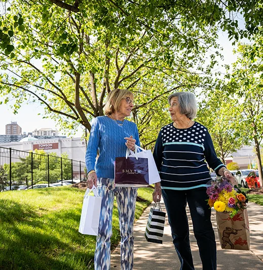 Edenwald_Inspired-Living Two active senior women walking down a sidewalk with shopping bags
