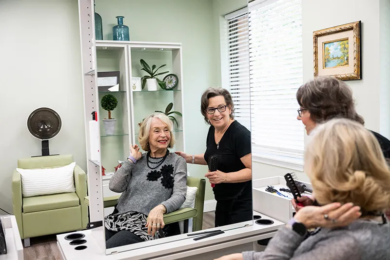Edenwald_Residential-Services-Amenities_1 A woman smiling looking at her new haircut in a mirror