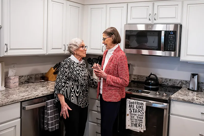 Two older women standing in an apartment kitchen talking