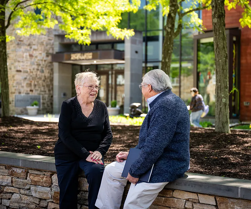 An older woman sitting outside a university building with a man