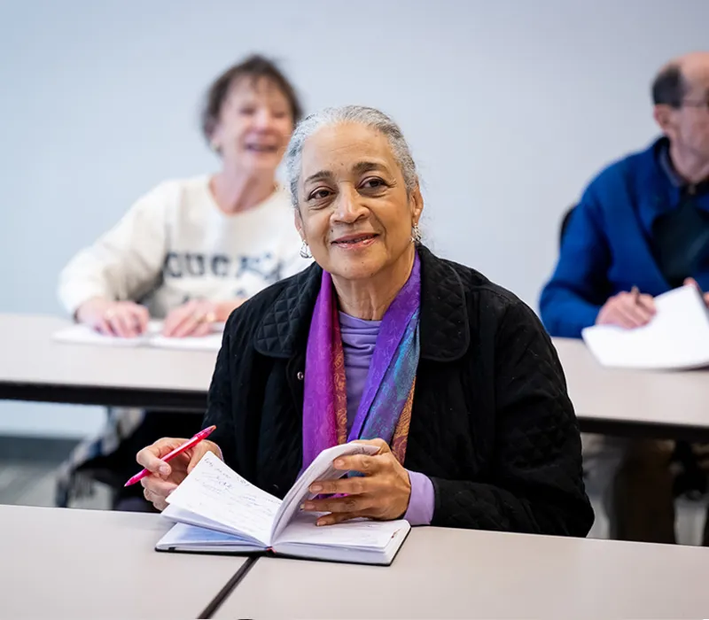 Edenwald_College-Enriched2 Woman smiling in a classroom with a notebook and pen