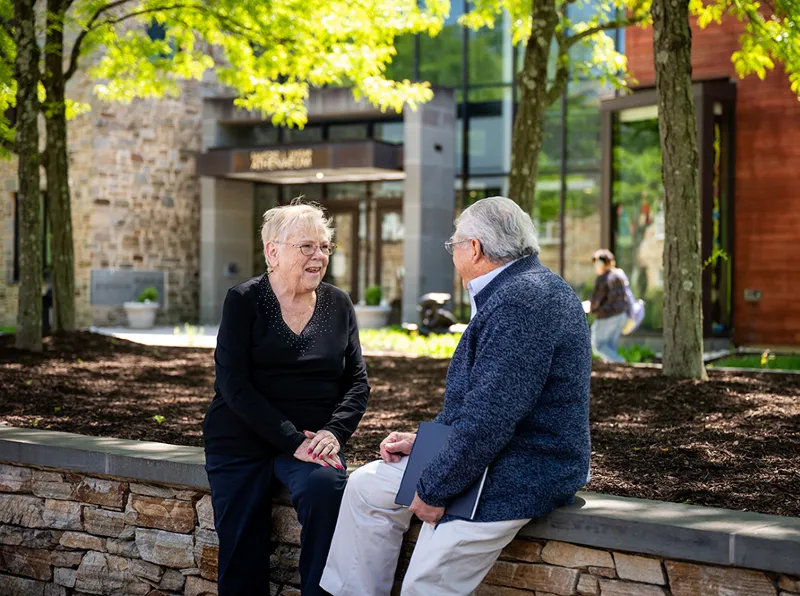 mission_values Woman sitting and talking to a man outside of a college building