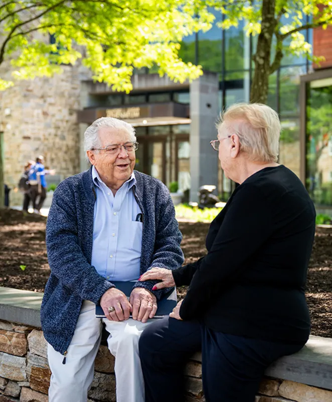 An elderly man and woman sitting outside a college talking